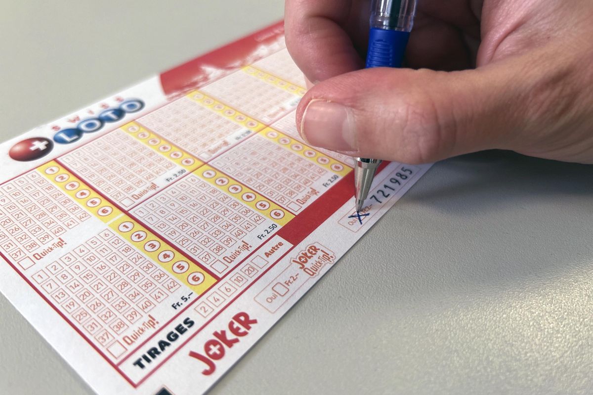 Une main tenant un stylo bleu remplit un bulletin de la Loterie Romande.