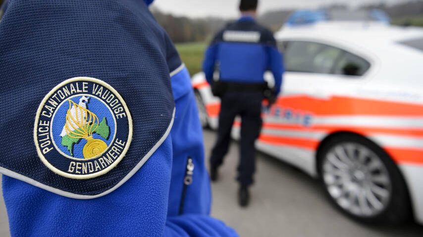 Deux agents de la police cantonale vaudoise en uniforme debout à côté d'une voiture de police.
