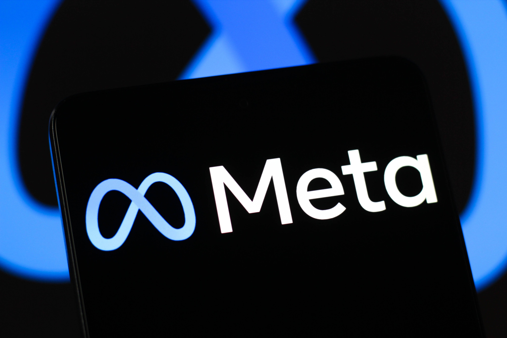 Meta-Platforms-Logo auf einem Smartphone-Bildschirm, blauer Hintergrund mit verschwommenem Meta-Symbol.