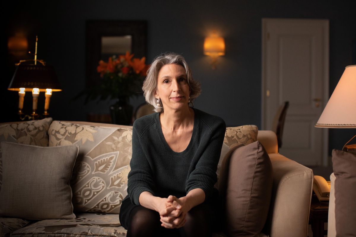 Mona Chollet assise dans la suite Coco Chanel au Lausanne Palace, avril 2022, entourée de coussins élégants.