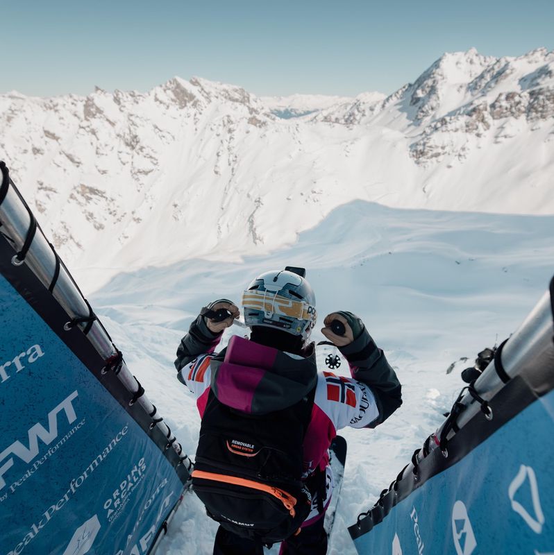 Snowboarder en haut d’une piste de descente enneigée avec des montagnes en arrière-plan.