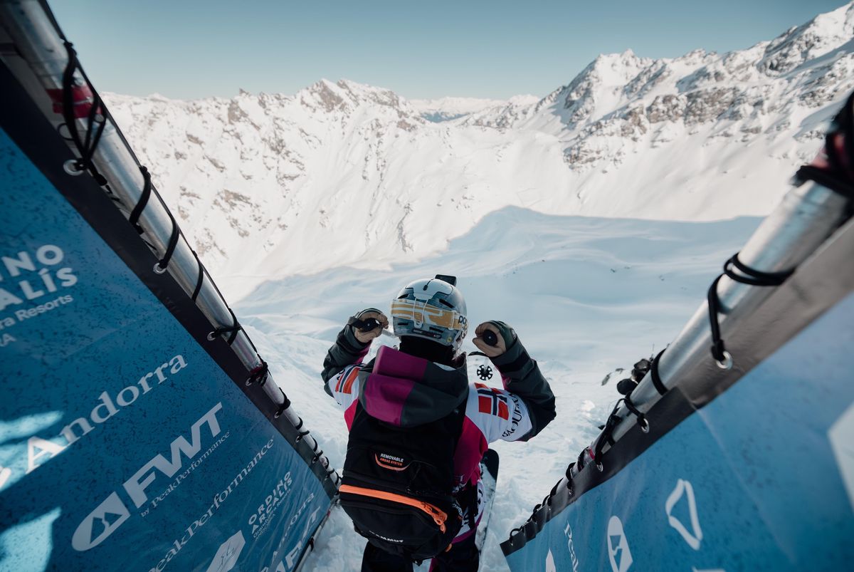 Snowboarder en haut d’une piste de descente enneigée avec des montagnes en arrière-plan.