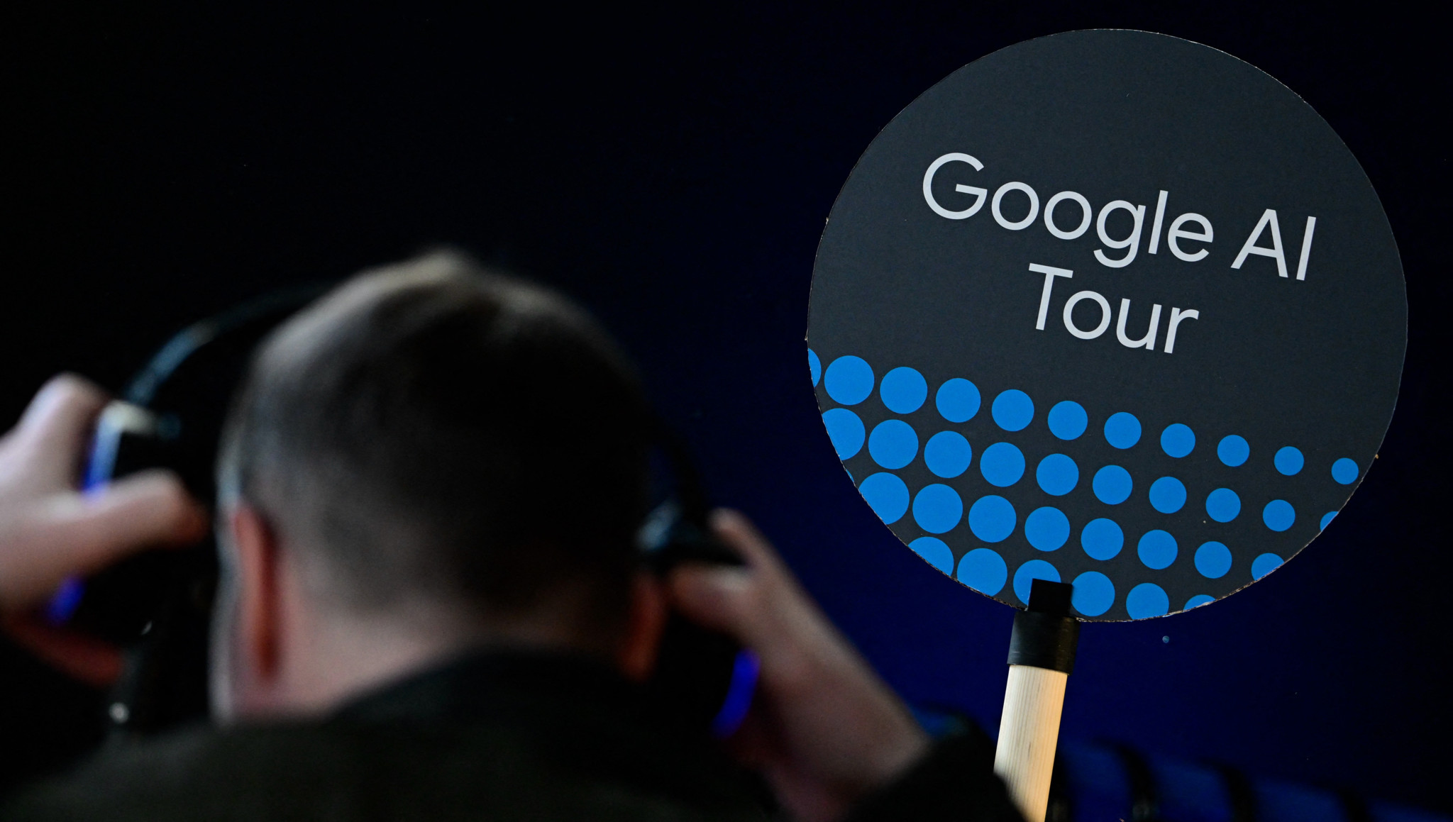 Un journaliste met un casque audio lors de l’ouverture du centre Google AI à Berlin, avec un panneau «Google AI Tour» visible au premier plan.