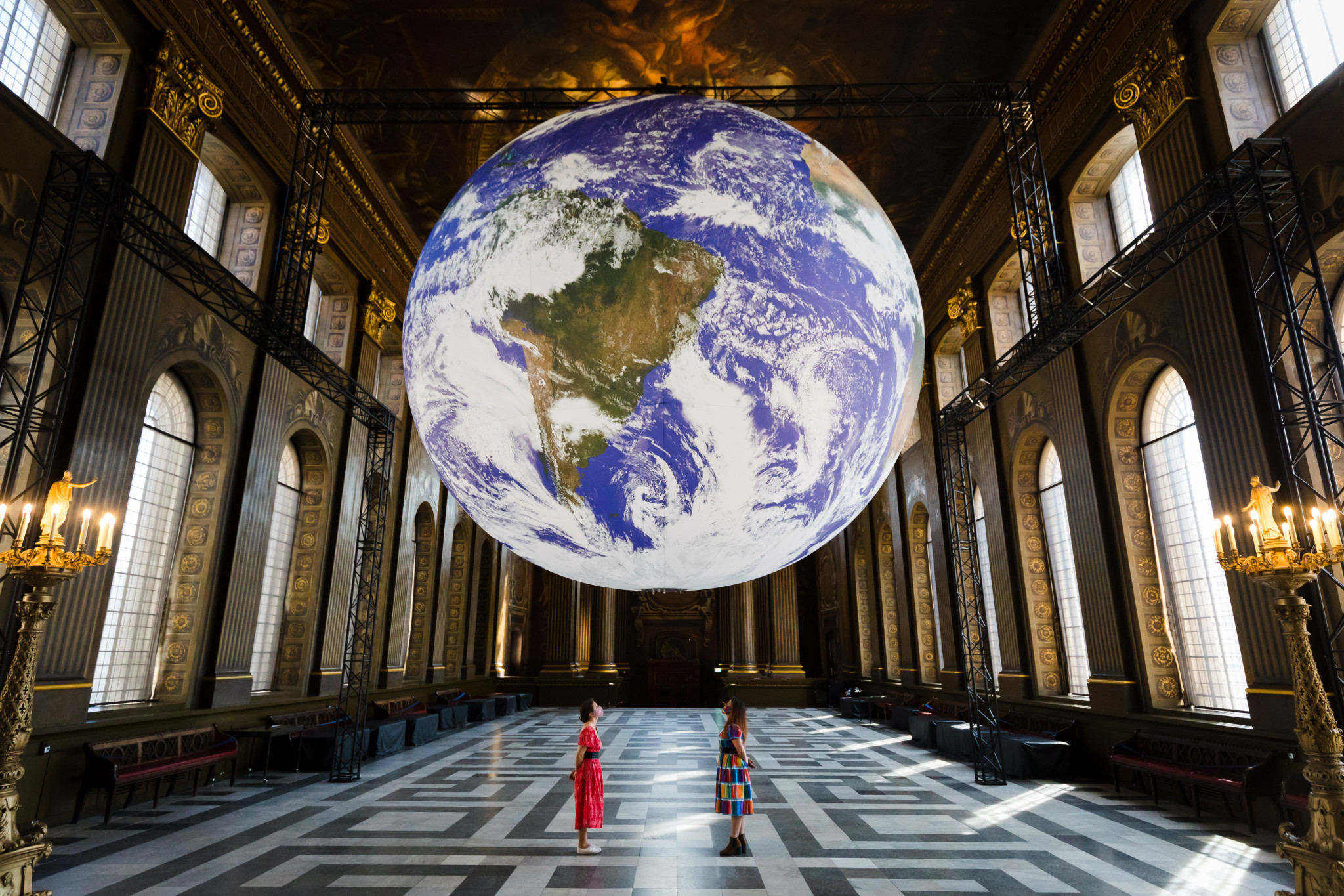 epa09240516 Members of staff pose with Luke Jerram's installation of a giant globe called 'Gaia' during a photocall at the Painted Hall in the Royal Naval College in Greenwich, London, Britain, 01 June 2021. The seven metre sculpture is an internally lit replica of the planet Earth using NASA imagery. It rotates and aims at replicating a sense of the 'Overview Effect' that astronauts experience when they see our home earth from space.  EPA/VICKIE FLORES