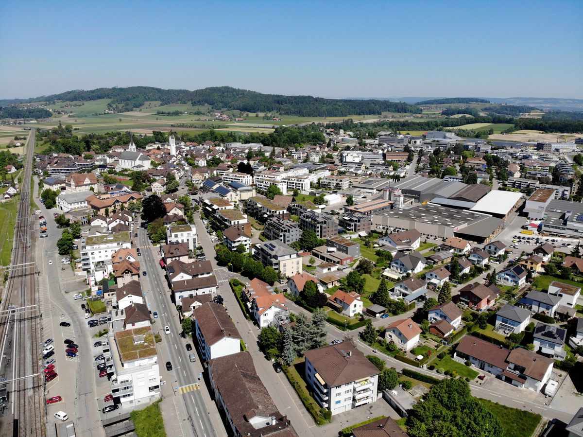 Luftaufnahme der Gemeinde Aadorf in der Schweiz, mit Blick auf Wohn- und Geschäftsgebäude sowie umliegende Landschaft.