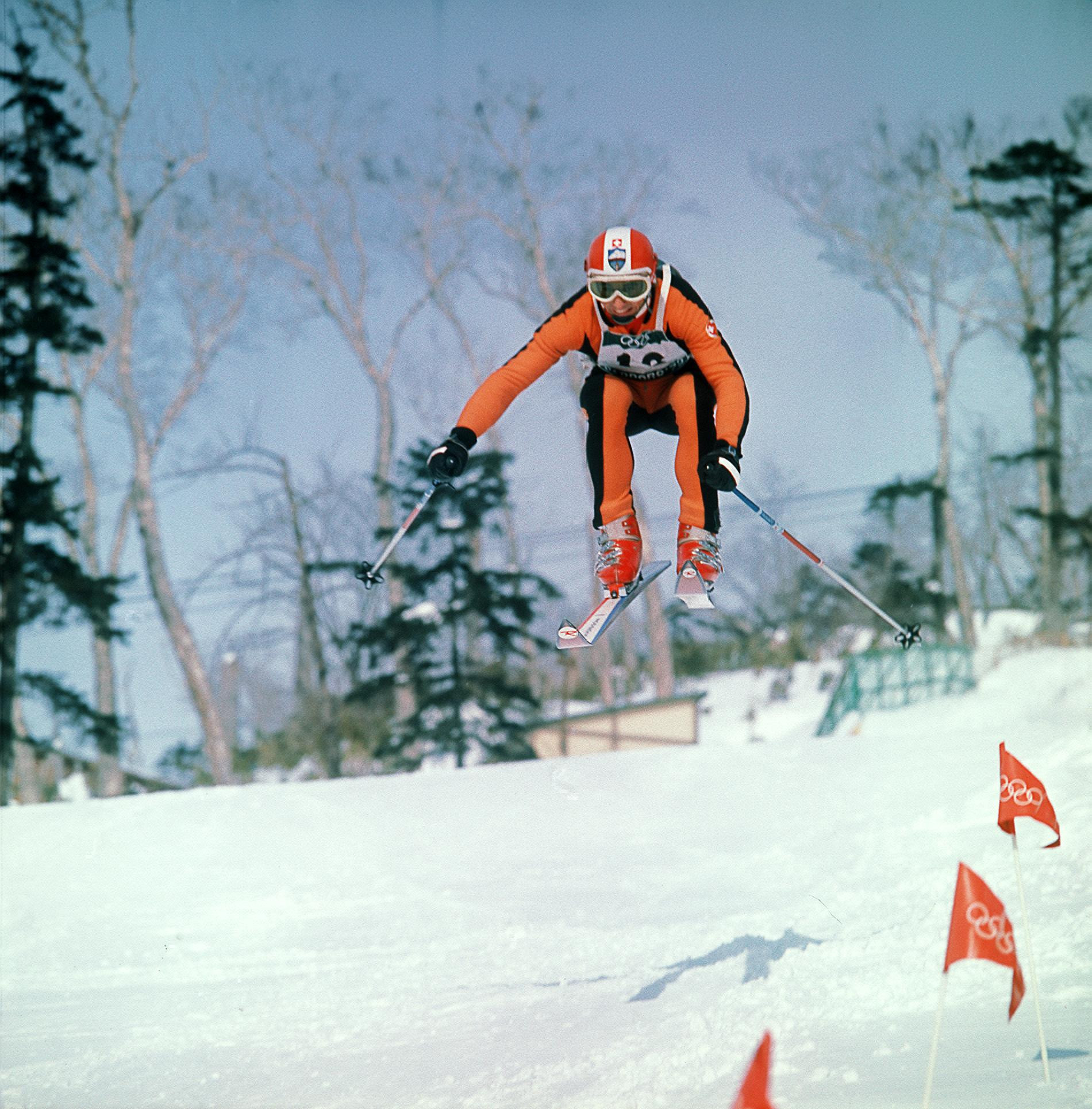 Walter Tresch in orangem Skianzug springt bei den Olympischen Winterspielen 1972 in Sapporo auf dem Weg zu Kombinations-Silber über eine Kuppe.