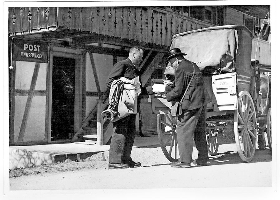 Historische Aufnahme einer Postkutsche vor der Post in Hinterfultigen, betreut von der Familie Marti seit 125 Jahren. Zwei Männer im Gespräch, einer überreicht dem anderen Post.