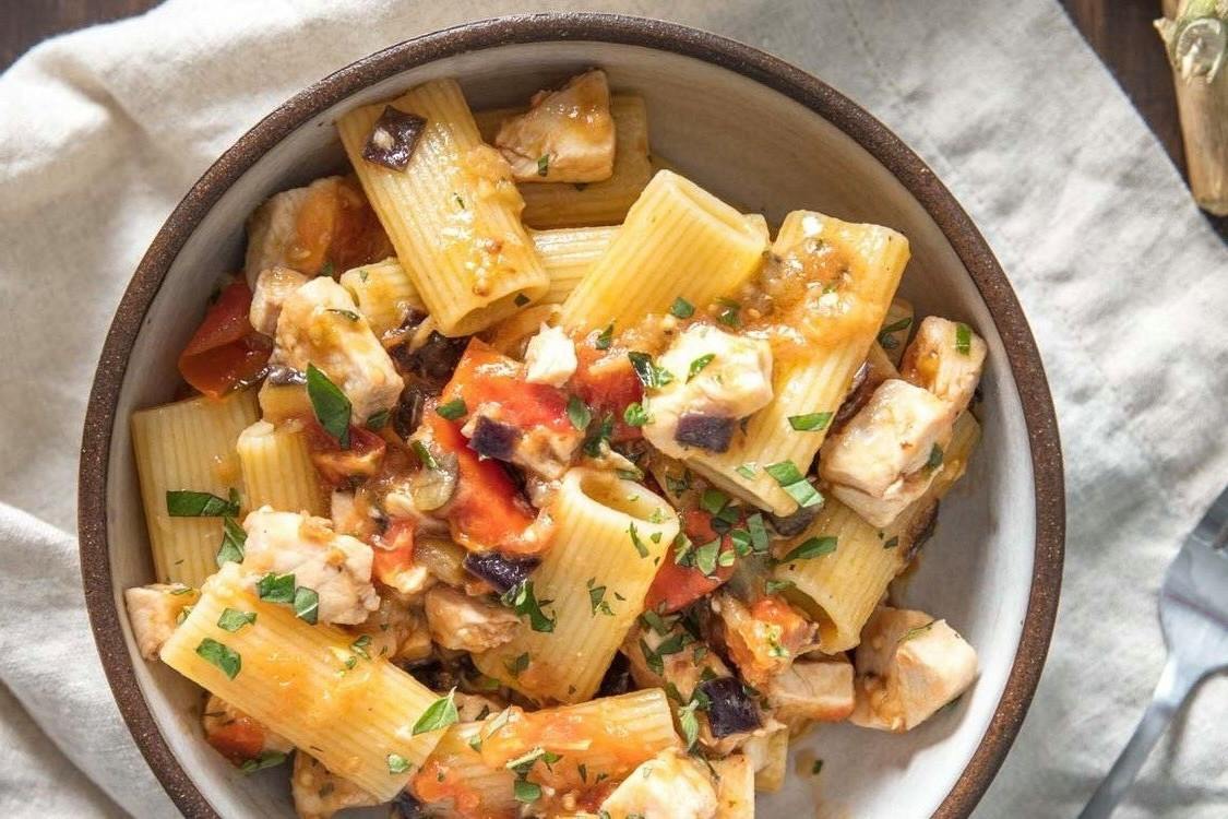 Rigatoni-Pasta mit Hühnchen, Auberginen, Tomaten und frischen Kräutern in einer Schüssel serviert.