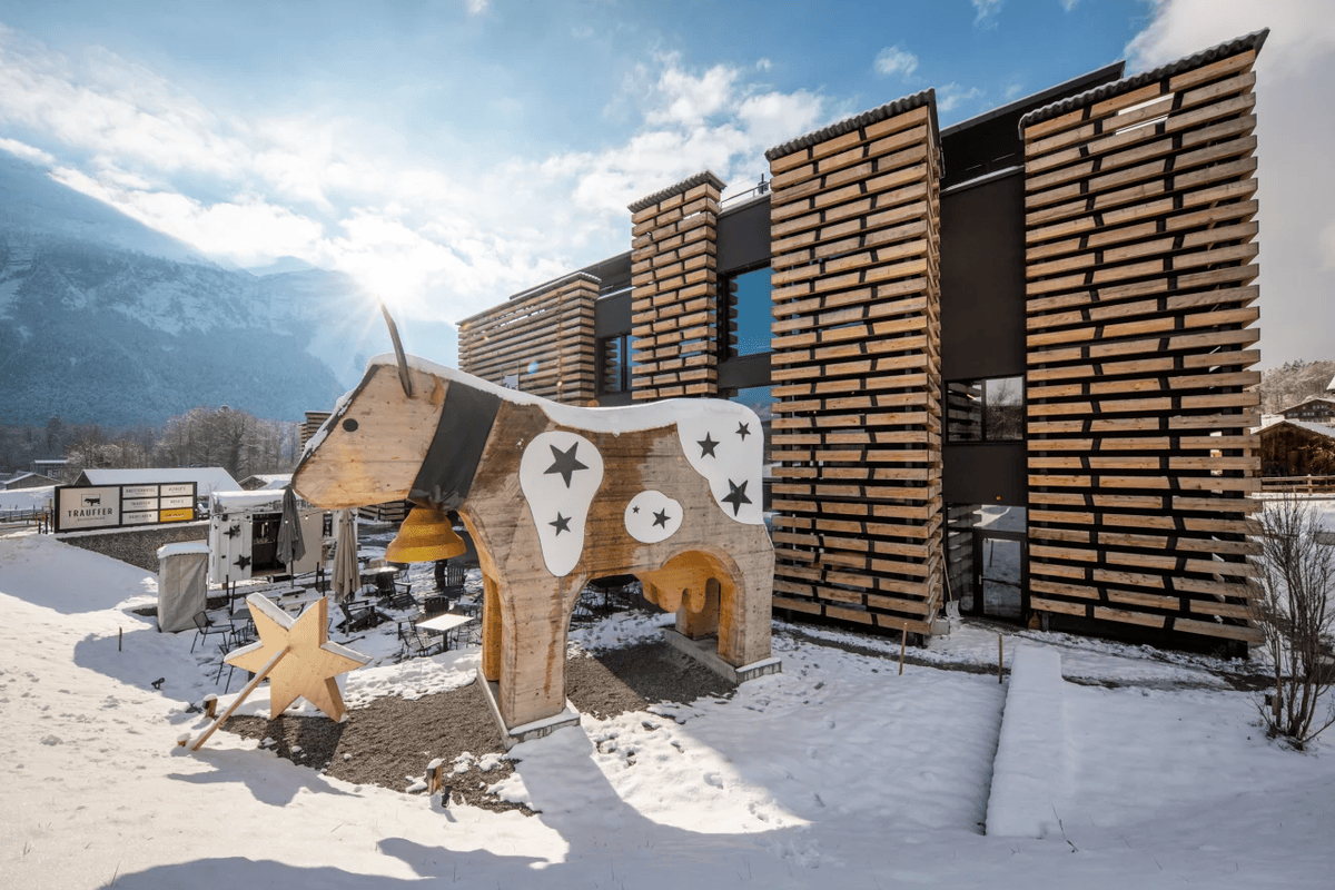 Grande sculpture de vache en bois du Bretterhotel, à Hofstetten (BE), décorée de motifs étoilés devant un bâtiment moderne dans un paysage enneigé de montagne.