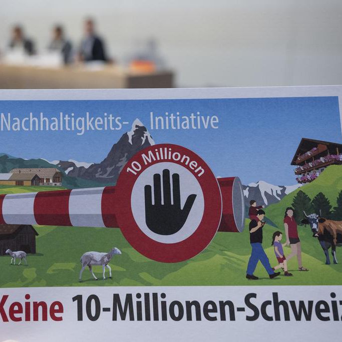 Un dépliant de l’initiative ’Aucune Suisse à 10 millions’ est tenu lors d’une conférence à Berne le 4 juillet 2023, avec des membres de la SVP en arrière-plan.