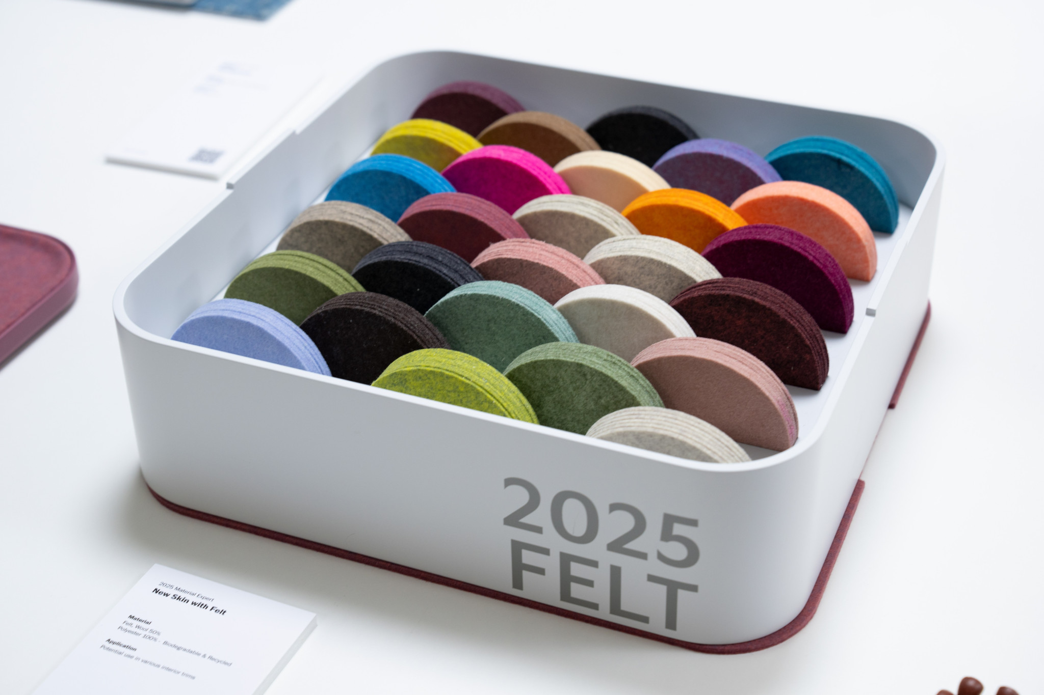 Weisse Box mit Aufschrift ’2025 FELT’ gefüllt mit bunten Filzmuster-Halbkreisen in verschiedenen Farben – nachhaltige Automaterialien.