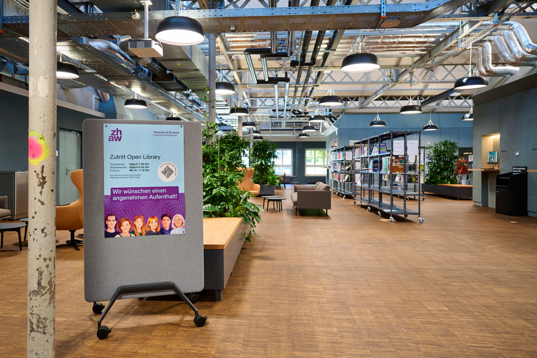 ZHAW-Campus in den umgebauten Shedhallen Wädenswil: Offene Bibliothek mit Bücherregalen, Pflanzen und Schild «Zutritt Open Library».