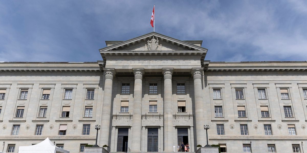 Façade du Tribunal Fédéral à Lausanne avec des colonnes imposantes, un escalier large et un drapeau suisse flottant au sommet.