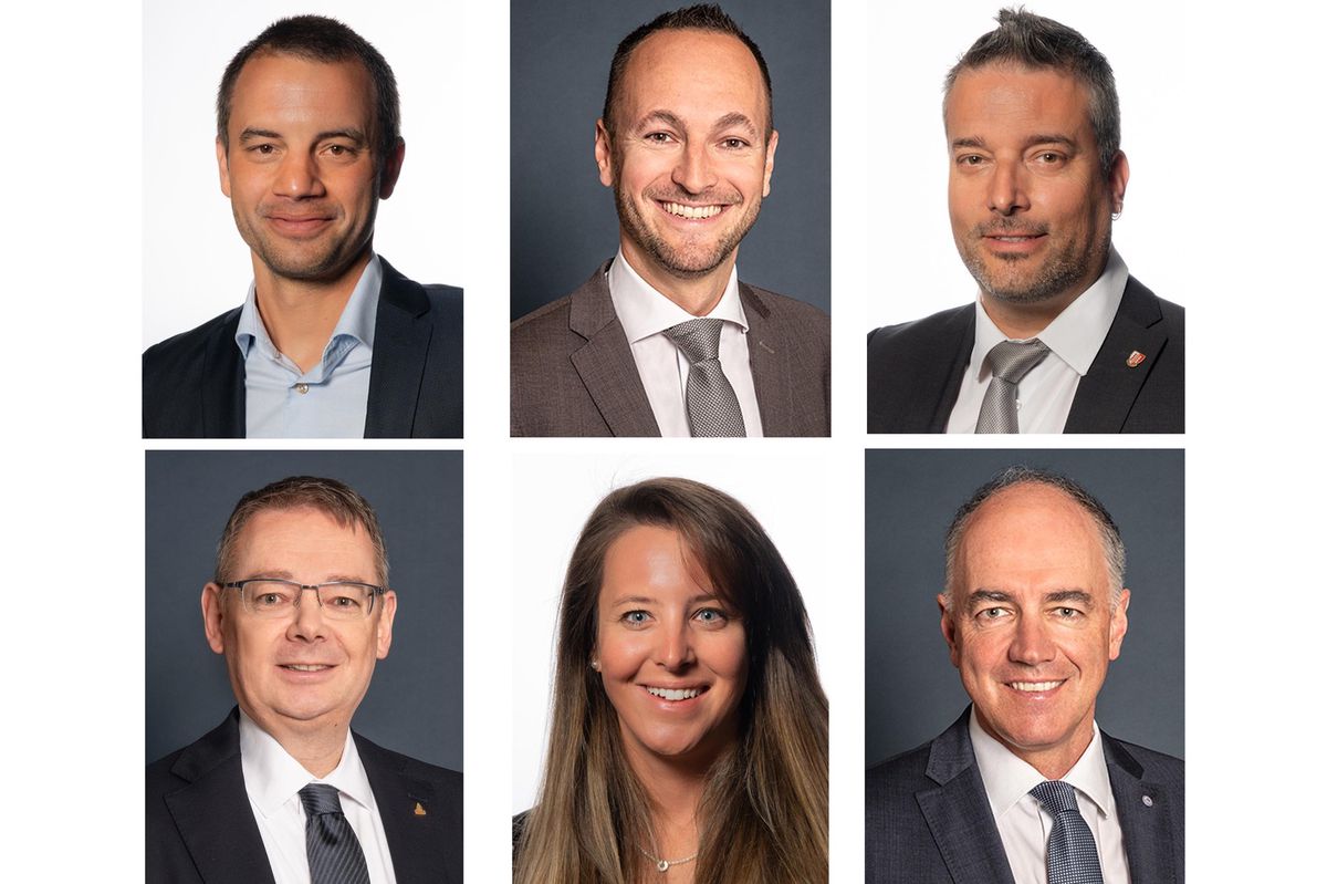 Six personnes portant des costumes, souriant face à la caméra, sur un fond gris foncé.