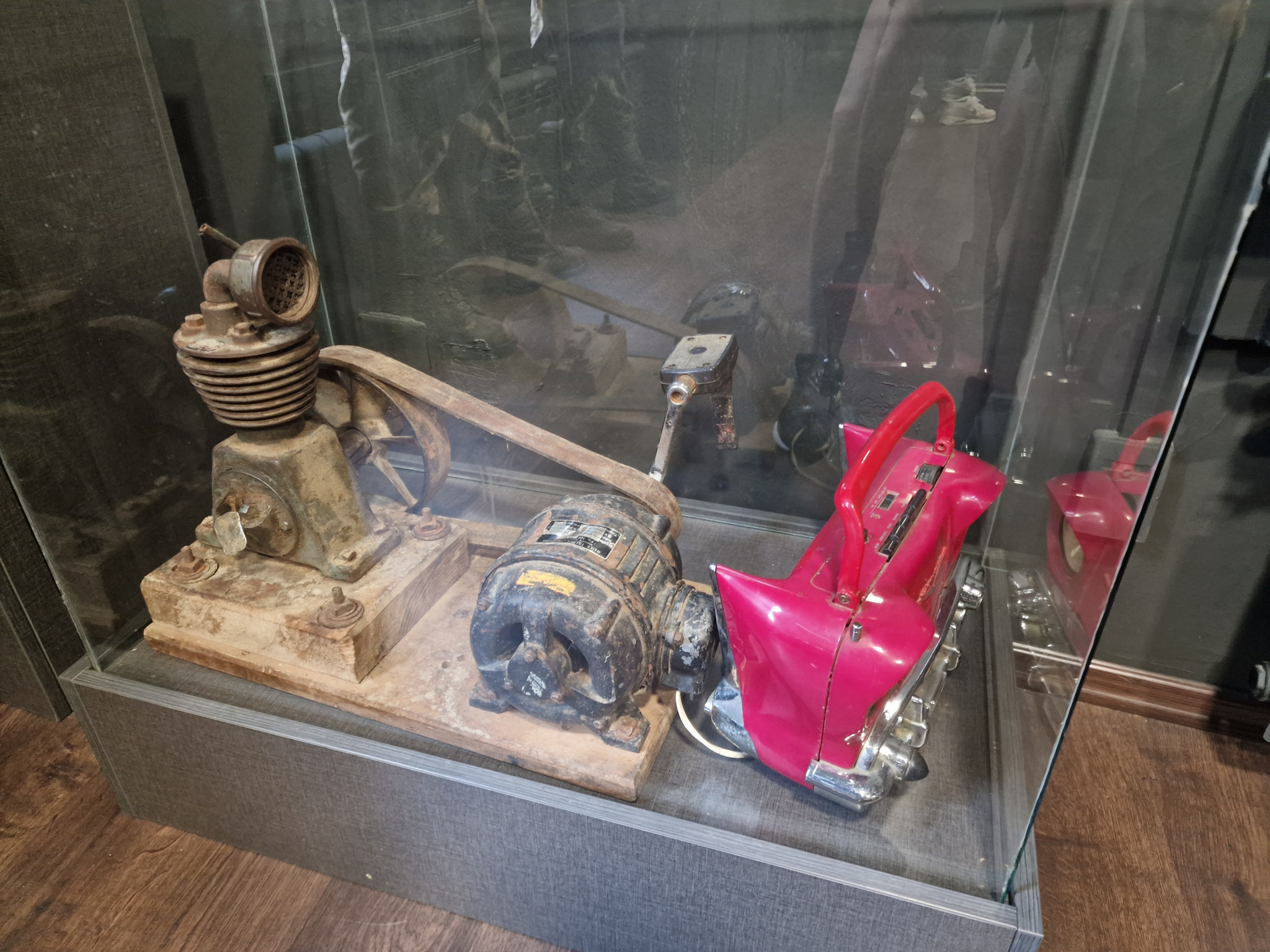 Eine Vitrine zeigt alte, rostige Maschinenbauteile neben einer auffallend roten, glänzenden Apparatur.