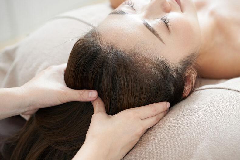 Femme allongée recevant un massage relaxant de la tête, visage détendu.