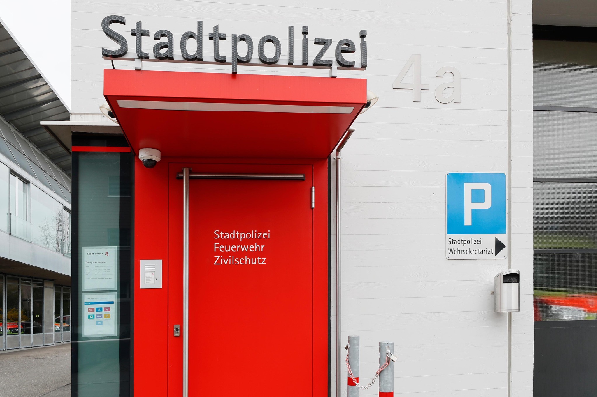 Eingang zur Stadtpolizei mit roter Tür und klarer Beschilderung für Feuerwehr und Zivilschutz neben einem Parkplatzschild.