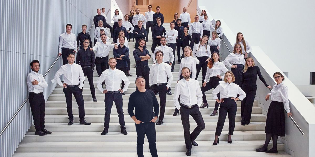 Le groupe Kristjan Järvi Ensemble pose sur un grand escalier, tous vêtus de chemises blanches et de pantalons noirs ou de jupes noires.