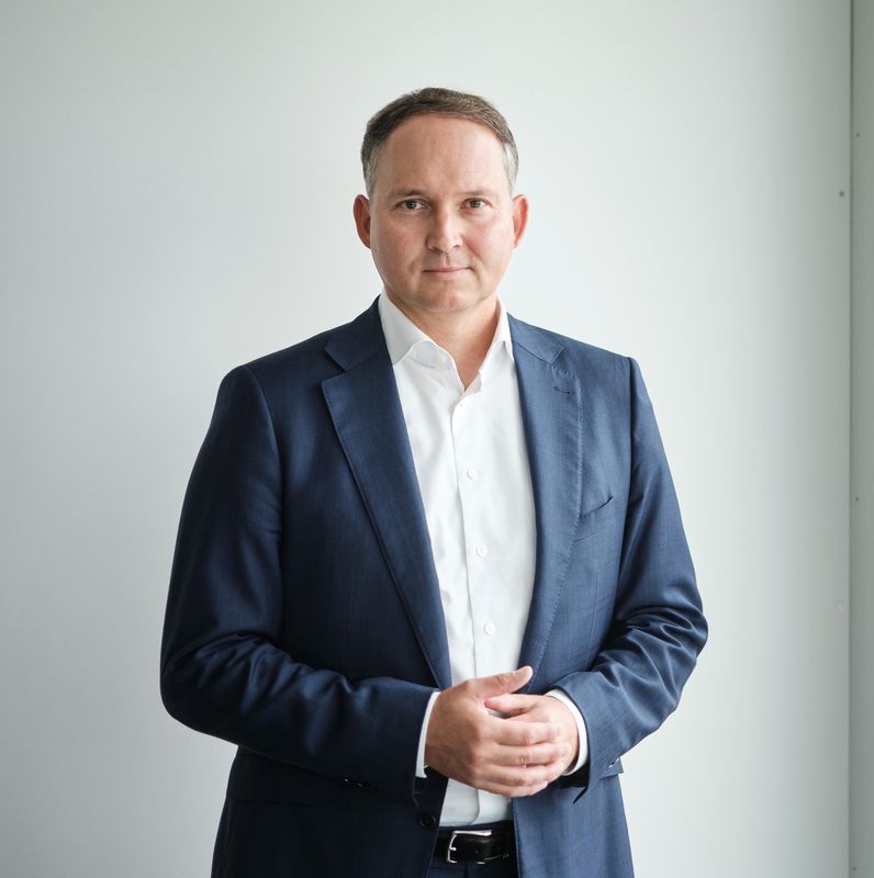 Ein Mann in einem dunklen Anzug steht vor einem Fenster. Er hat kurze Haare und trägt ein weisses Hemd.