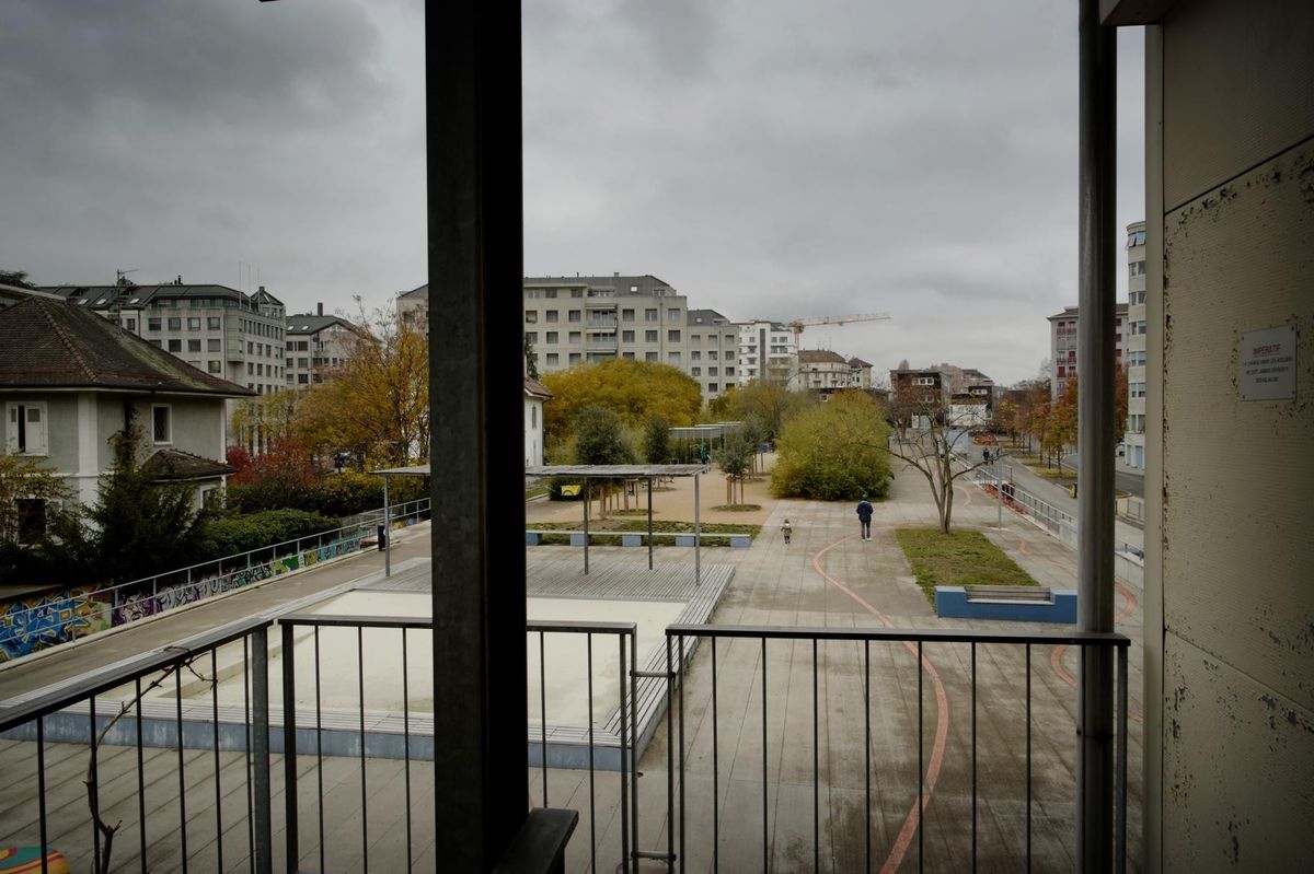 Vue d'une place publique vide avec quelques bâtiments résidentiels en arrière-plan par un jour nuageux.