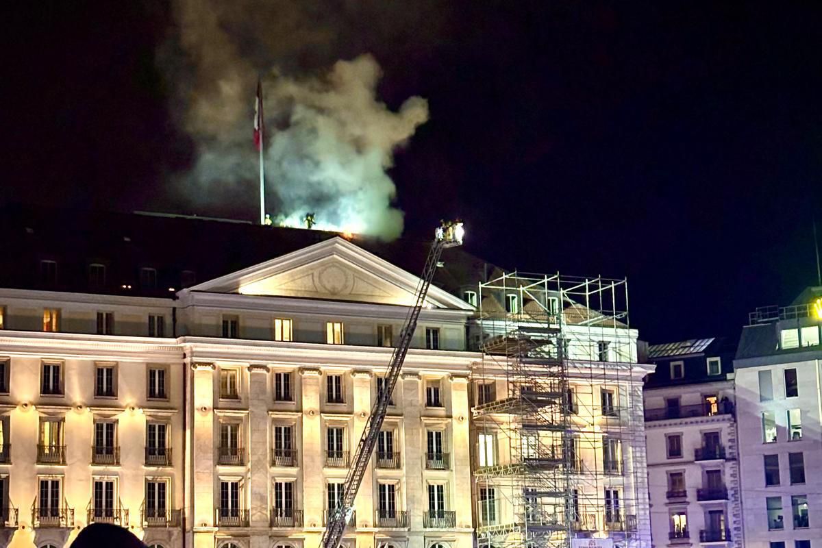 Bâtiment historique en feu avec de la fumée s’échappant du toit, des échelles de pompiers visibles, et spectateurs observant la scène la nuit.