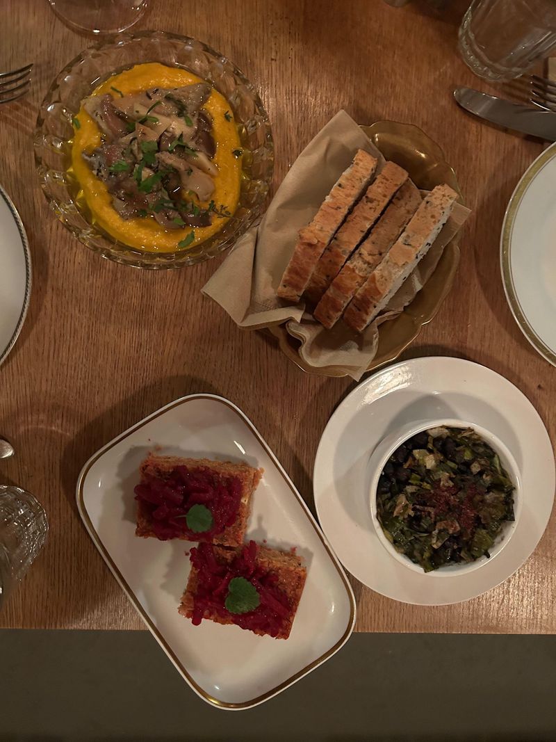 Eine Auswahl an Speisen auf einem Holztisch, darunter Brot, Fisch auf gelbem Püree, rote Vorspeise und Beilagen in Schüsseln.