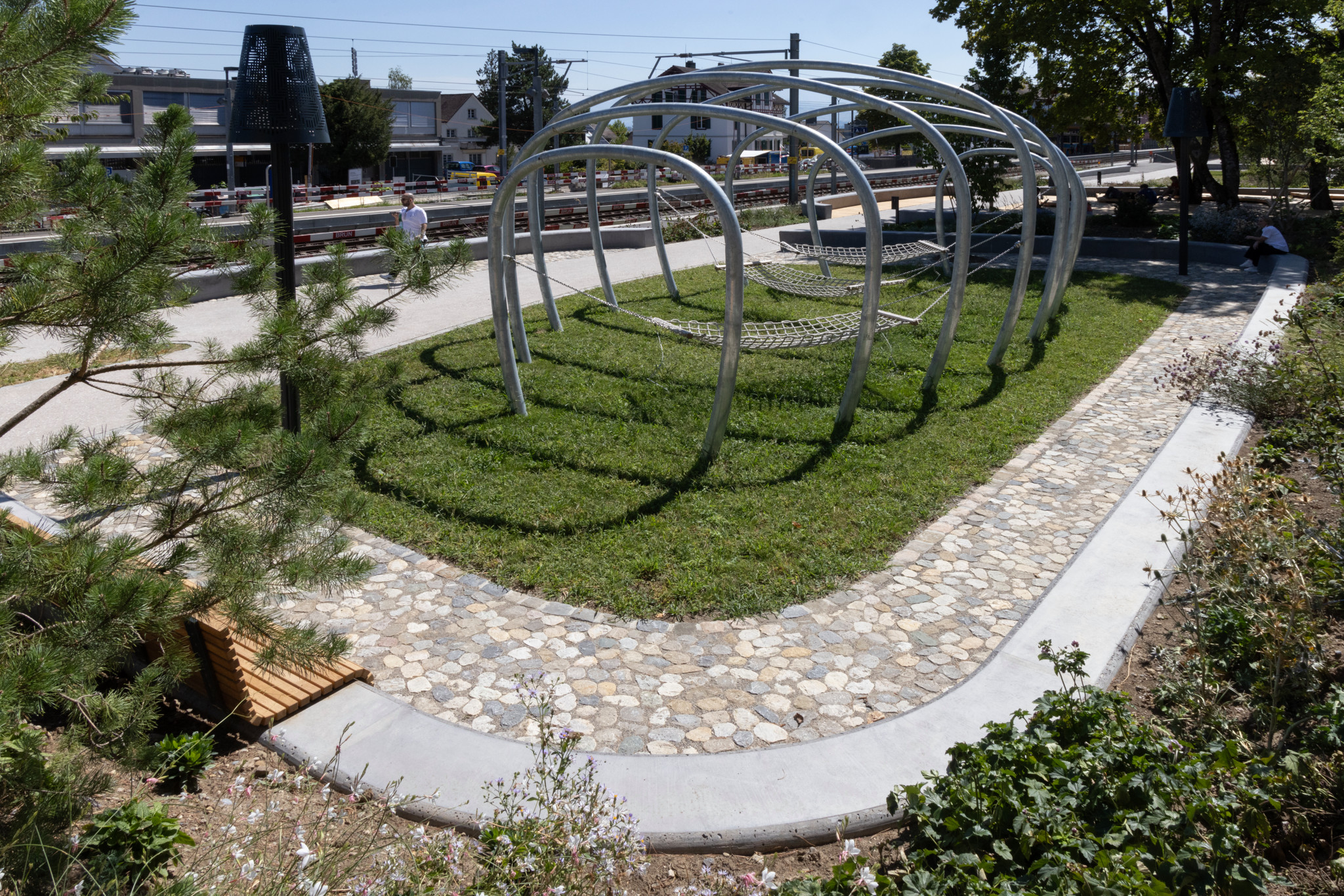 Neu eröffneter Weingartenpark in Rüschlikon oberhalb des Bahnhofs mit geschwungenem Kopfsteinpfad, Metallbögen und Grünflächen.