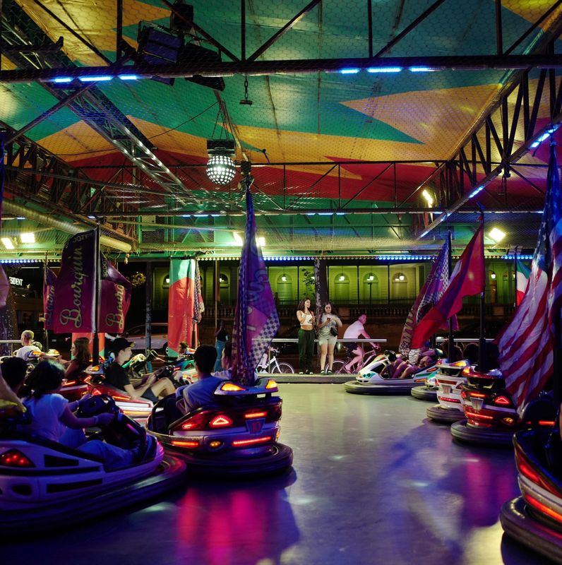 Autos tamponneuses illuminées à la fête foraine sur les quais de Genève, avec des drapeaux colorés et des visiteurs enthousiastes.