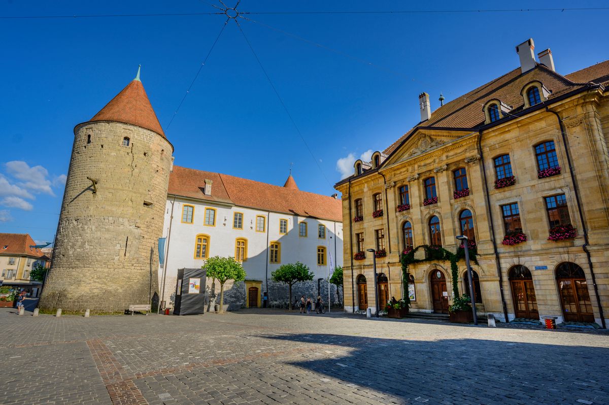 Place Pestalozzi à Yverdon-les-Bains, montrant le château médiéval et l'Hôtel de Ville sous un ciel bleu.