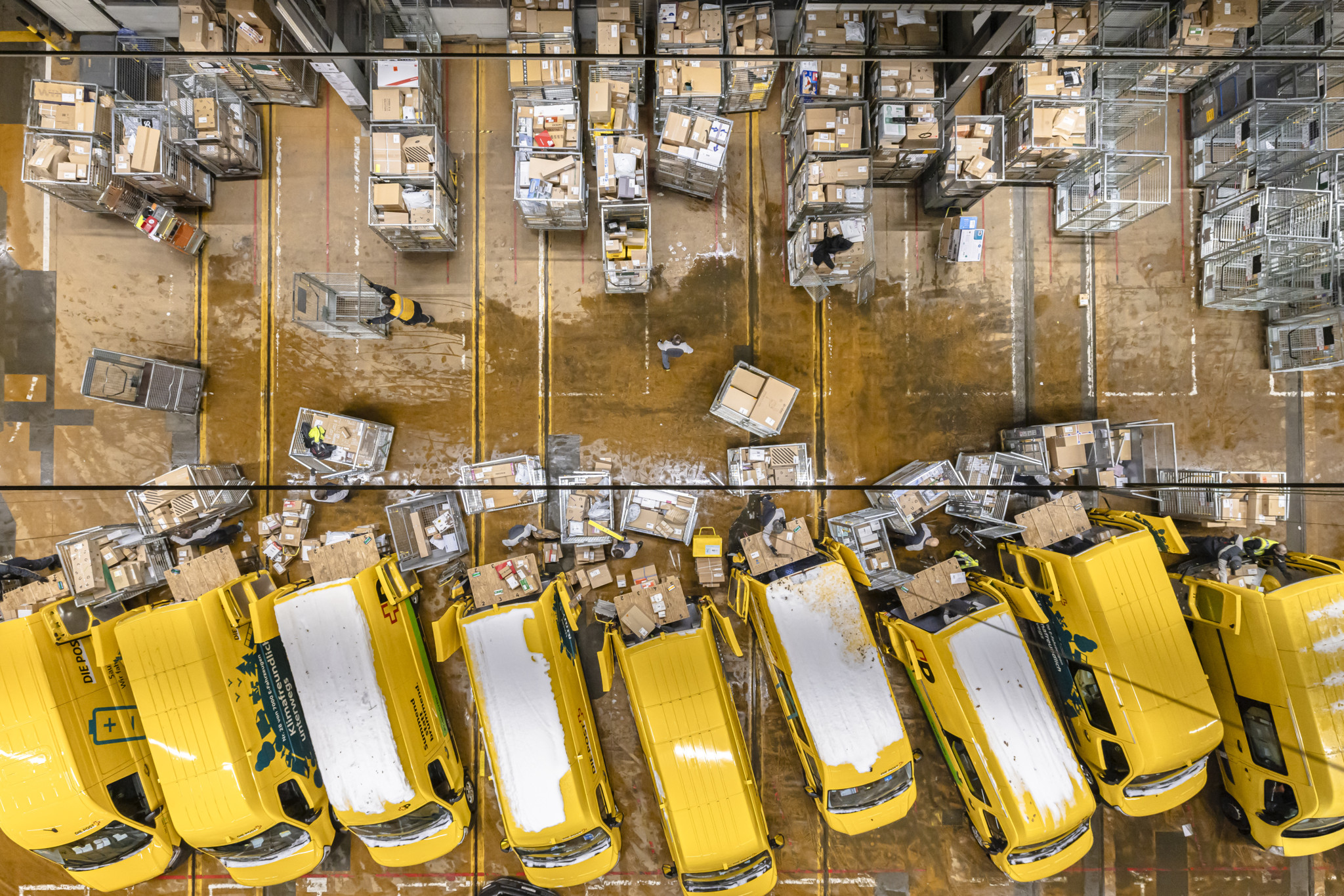 Luftaufnahme der Distributionsbasis Oerlikon: Paketboten der Schweizerischen Post beladen gelbe Lieferwagen mit Paketen.