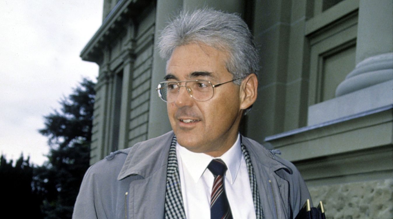 Félix Glutz, portant un manteau gris et une cravate, arrive au tribunal avec des documents.