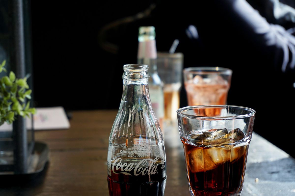 Verres et bouteille de Coca-Cola sur une table, avec des boissons gazeuses en arrière-plan.
