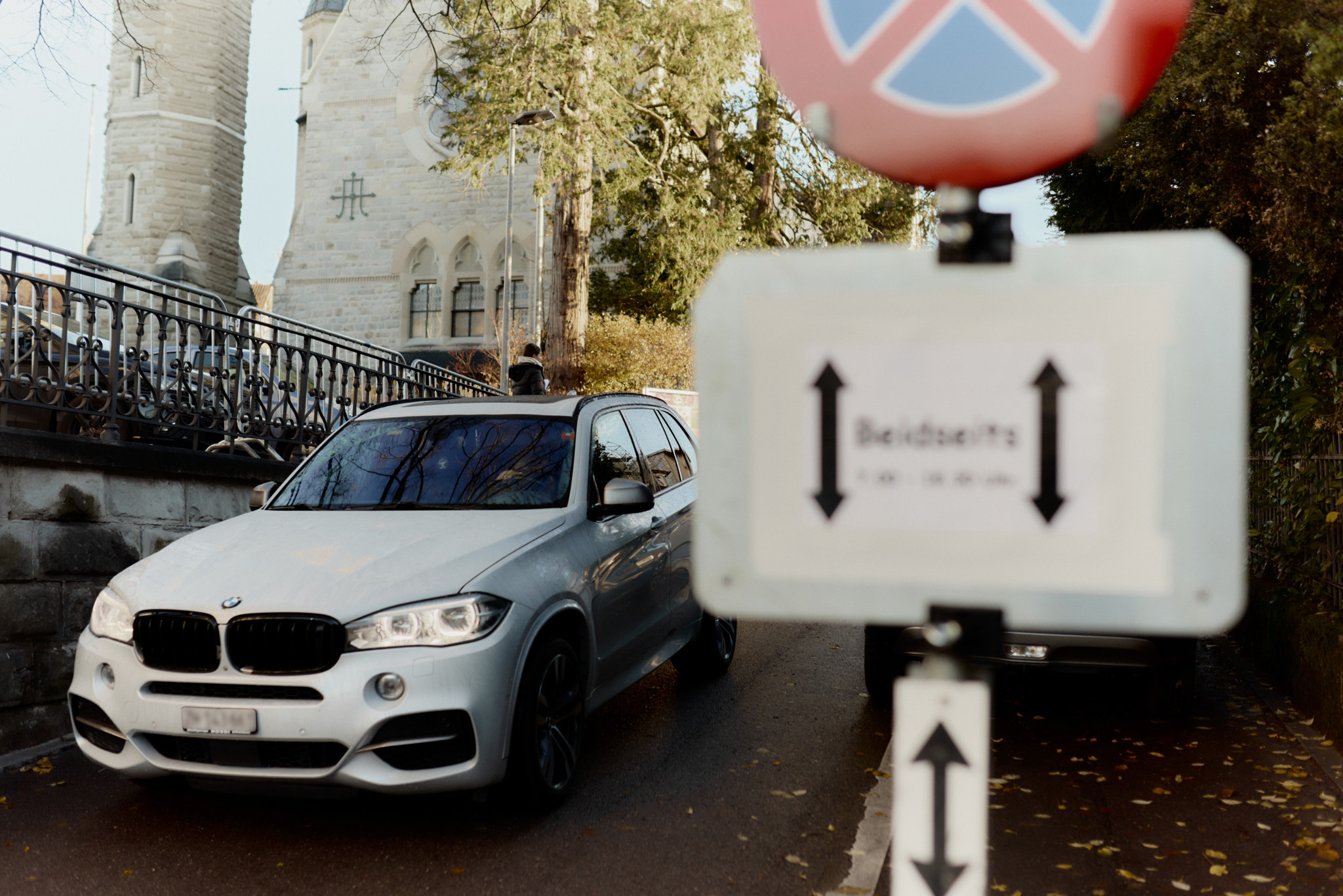 Halteverbotsschild mit Zusatztafel «Beidseitig» vor der Primarschule Männedorf, daneben ein weisser BMW SUV (Elterntaxi).