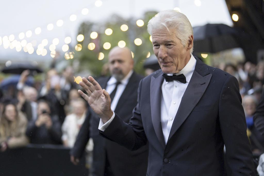 Un homme en smoking salue sur le Green Carpet du 20ème Zurich Film Festival, entouré de lumières et de spectateurs.