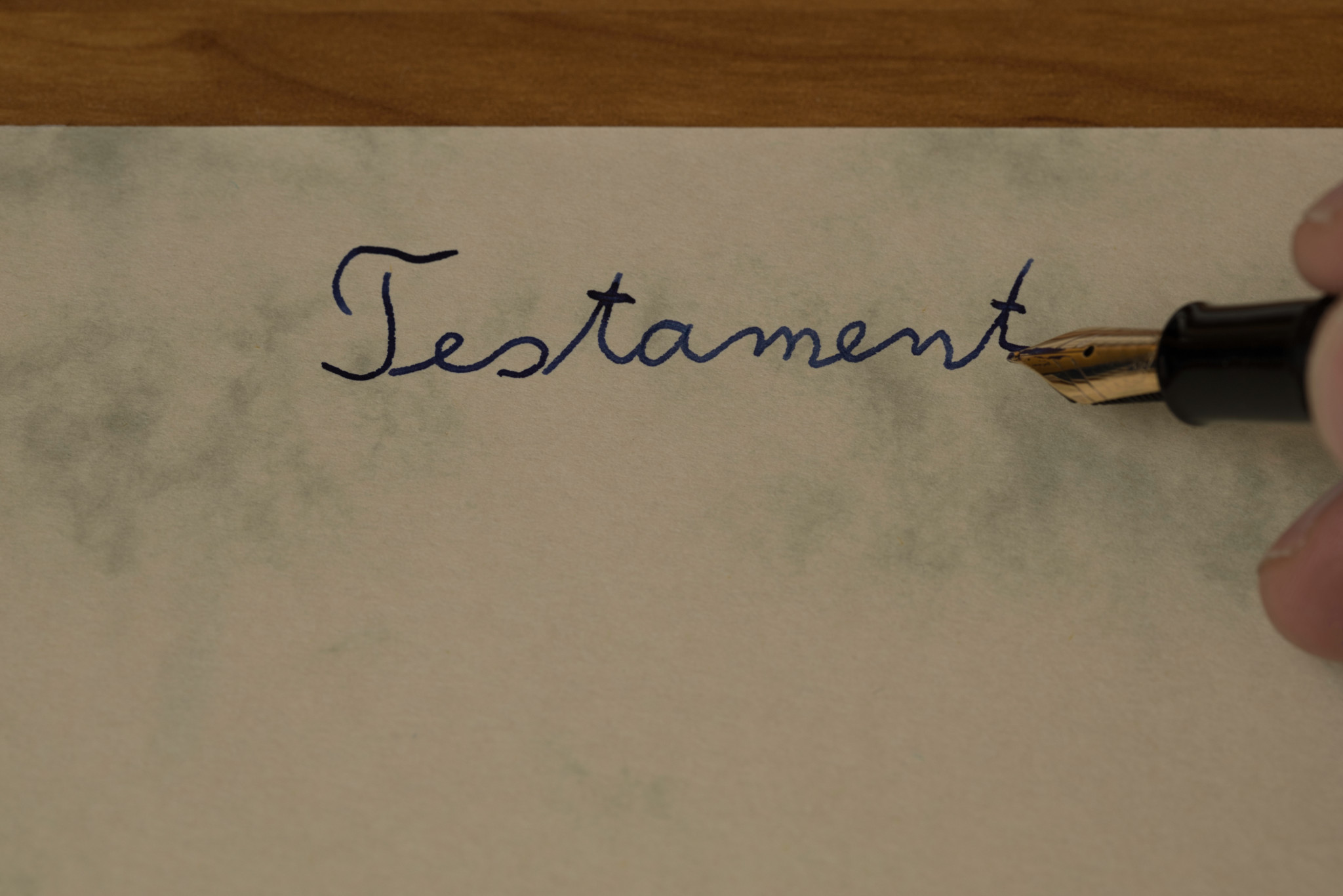 male hand writing german word Testament, translation last will, with a golden fontain pen, ink pen