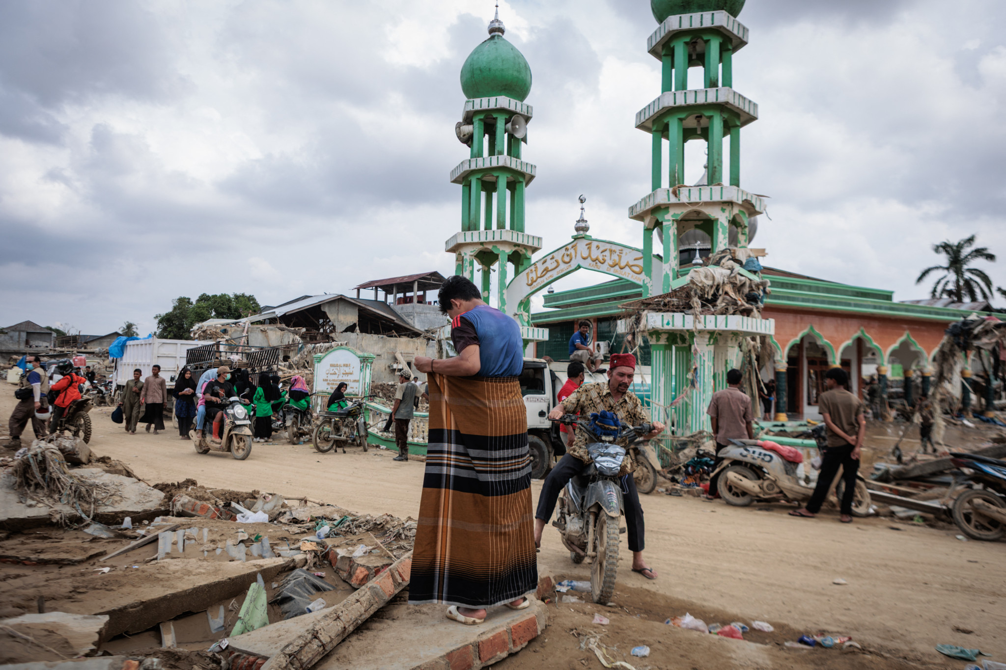 Un homme musulman se prépare pour la prière du vendredi devant la mosquée Al Ihsan, partiellement endommagée par des inondations à Aceh Tamiang, Sumatra Nord, le 12 décembre 2025. Des dégâts sont visibles autour.