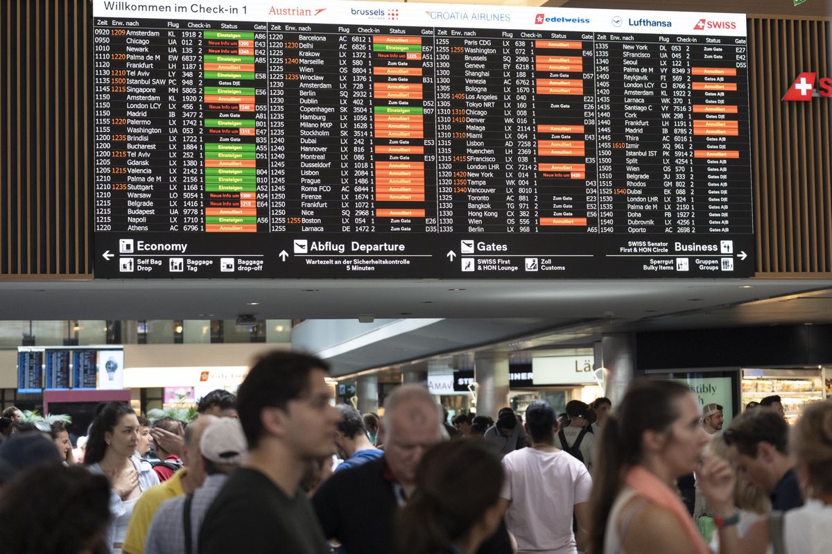 Passengers look at screens informing them of the flight situation, on Friday, 19 July 2024, at the airport Zurich in Kloten, Switzerland. Due to a worldwide IT breakdown, check-in for air travellers and flight operations are severely restricted and most flights are delayed or cancelled.  Swiss air traffic control Skyguide is also affected by the IT disruption and has reduced the capacity of Swiss transit traffic as an immediate precautionary measure. (KEYSTONE/Gaetan Bally)