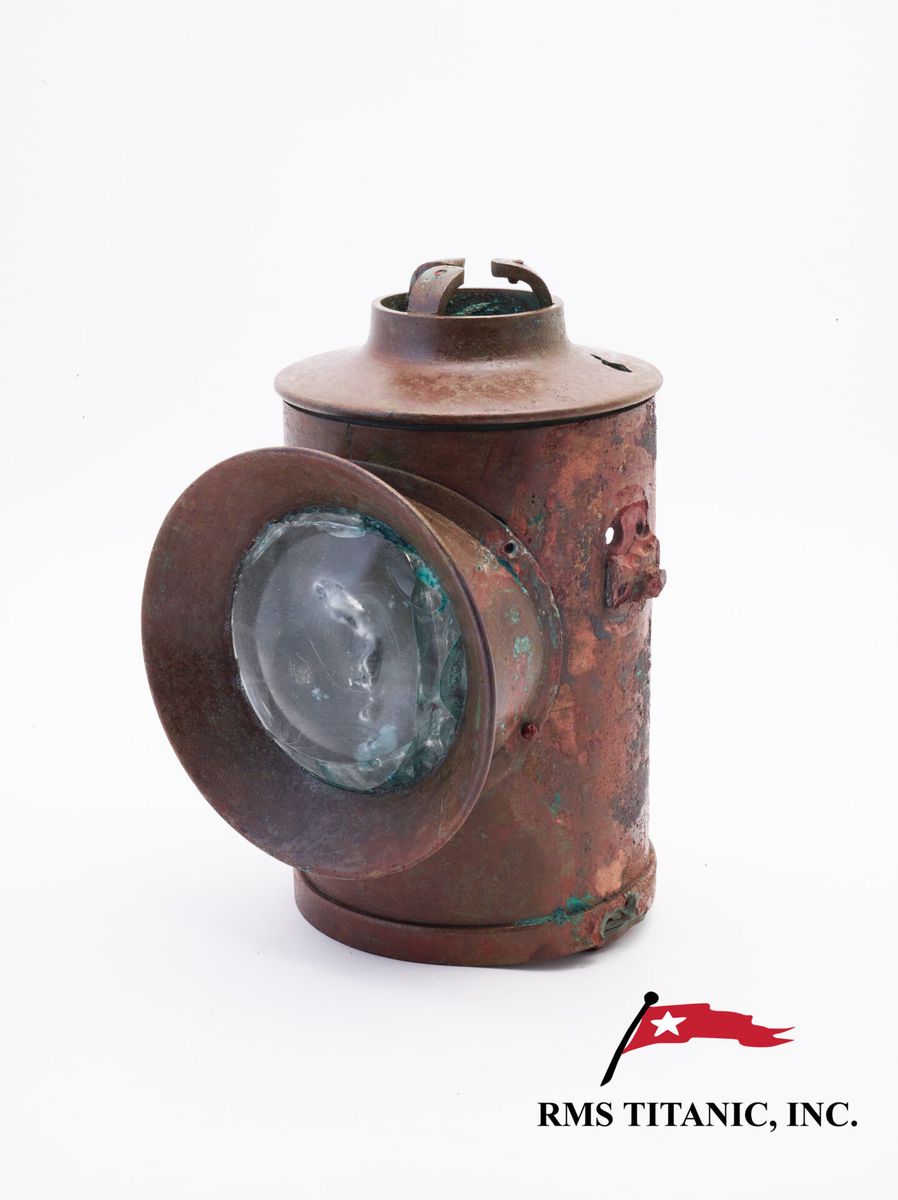 Lanterne en cuivre avec lentille en verre, provenant du RMS Titanic, exposée sur un fond blanc avec le logo RMS Titanic, Inc.