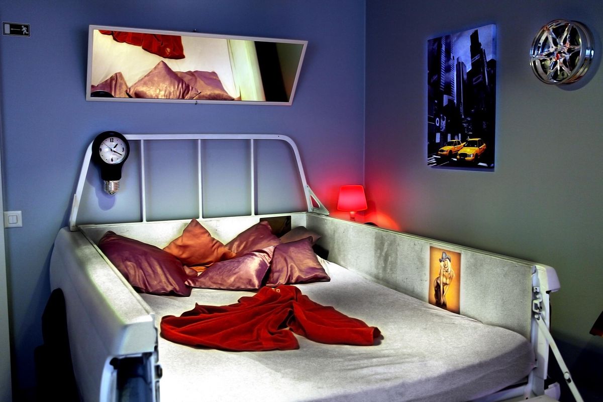 Chambre du salon de massage Venusia à Genève avec un lit, des coussins rouges, et des décorations murales.