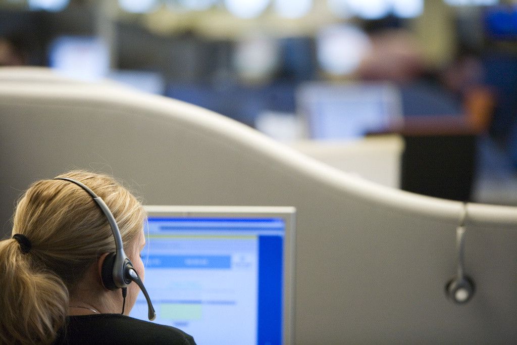 Employé de bureau portant un casque, travaillant sur un ordinateur avec un écran bleu ouvert, dans un centre d'appels animé.