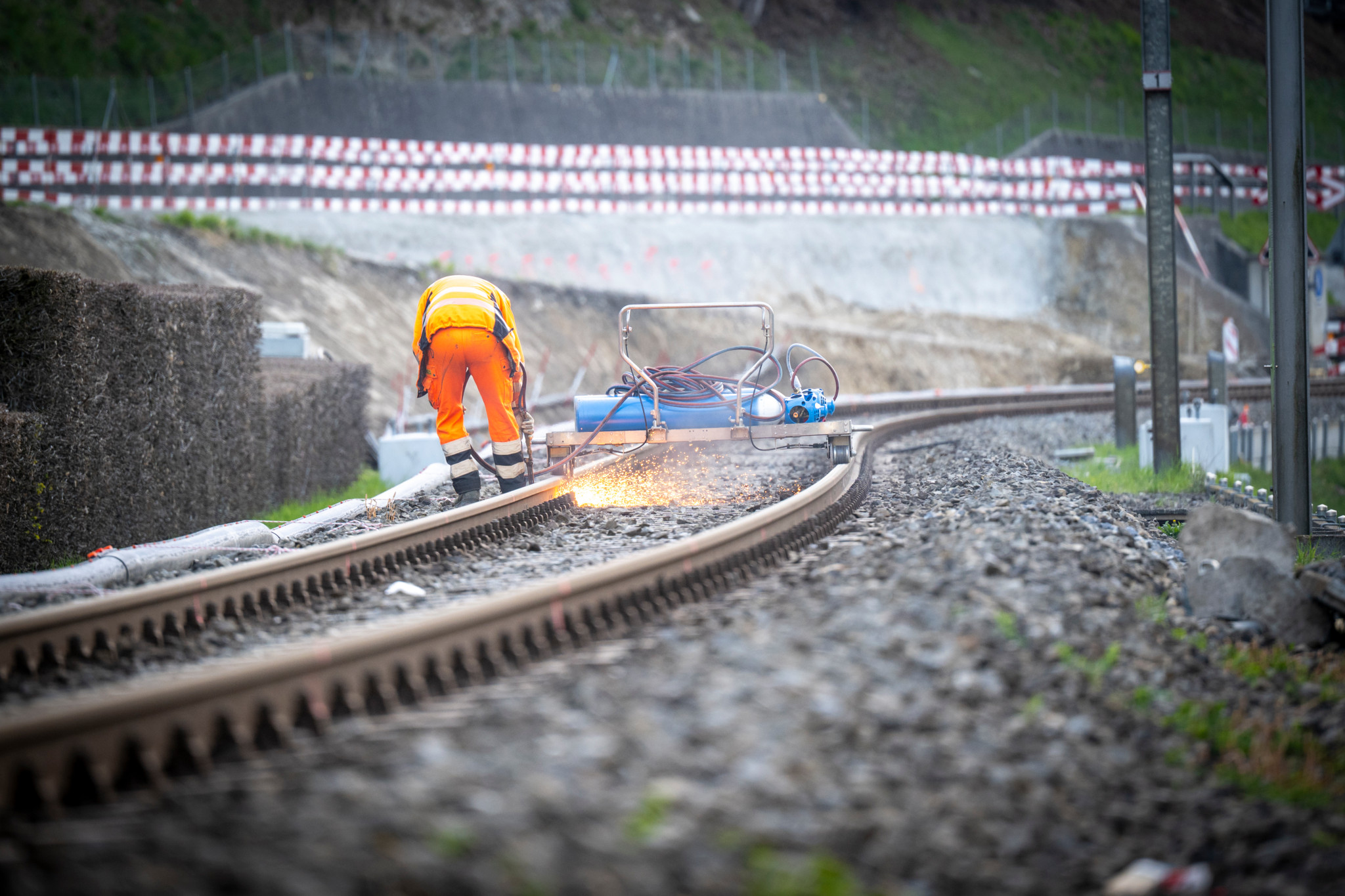 Bauarbeiten an der Bahnstrecke Trubschachen, umgeben von Bahnenschildern. Arbeiter in orangener Arbeitskleidung führt Arbeiten auf den Gleisen durch. Foto von Marcel Bieri.