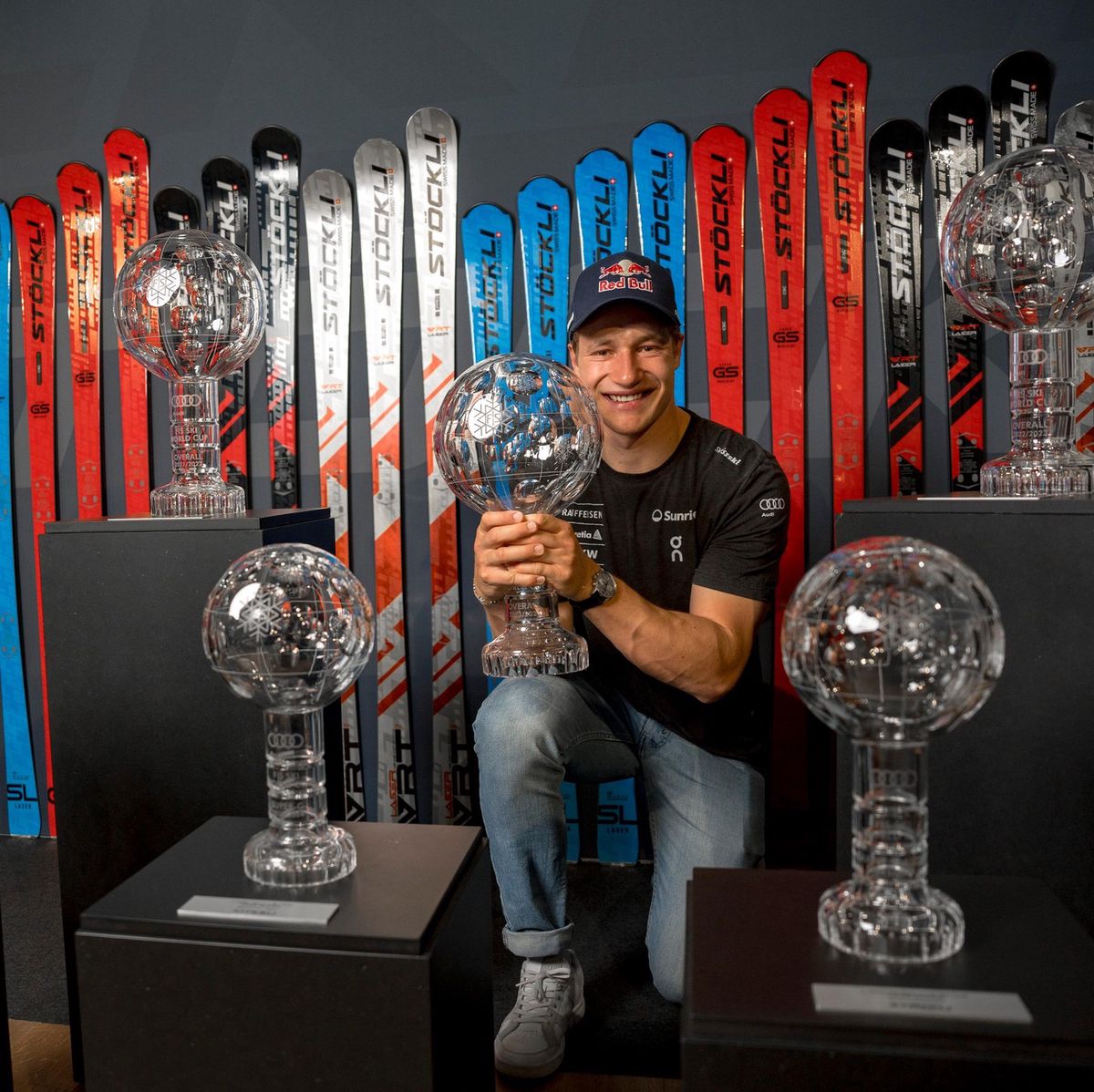 Marco Odermatt posant avec plusieurs trophées de cristal devant une rangée de skis Stöckli lors d’une conférence de presse à Engelberg.