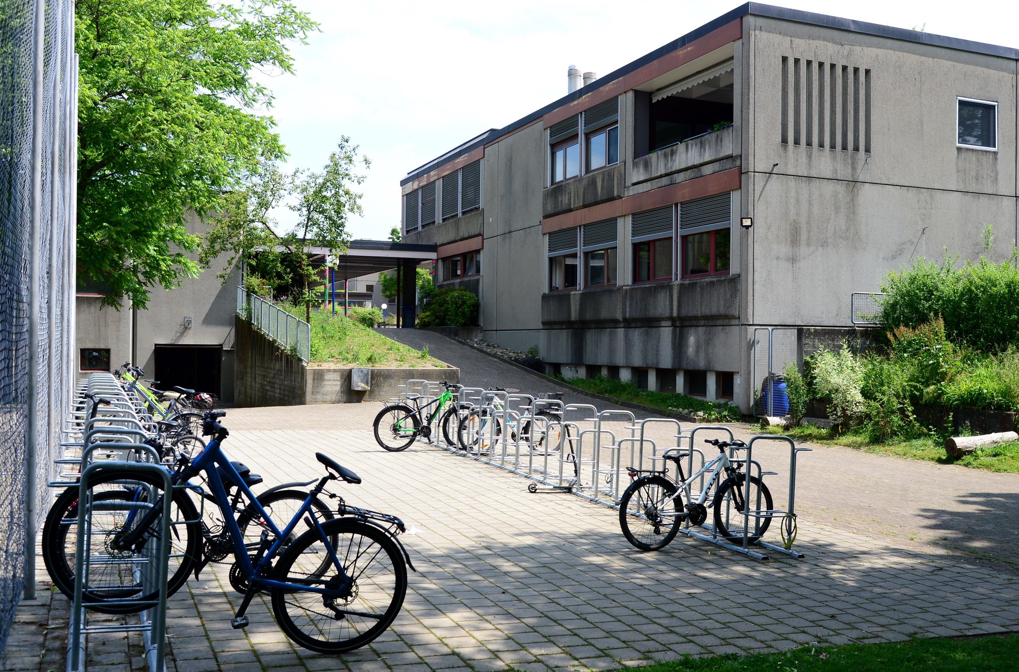 Mehrere Fahrräder sind vor dem Schulhaus Stenacker in Winterthur geparkt, im Hintergrund ist das grosse Betongebäude sichtbar. Foto aufgenommen am 2. Juni 2022.