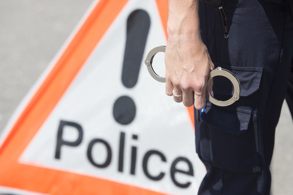 Un policier tient des menottes devant un signe police