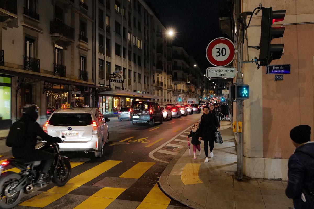 Circulation dense en soirée sur le Boulevard du Pont-d'Arve à Genève, avec une zone limitée à 30 km/h. Des piétons marchent sur le trottoir.
