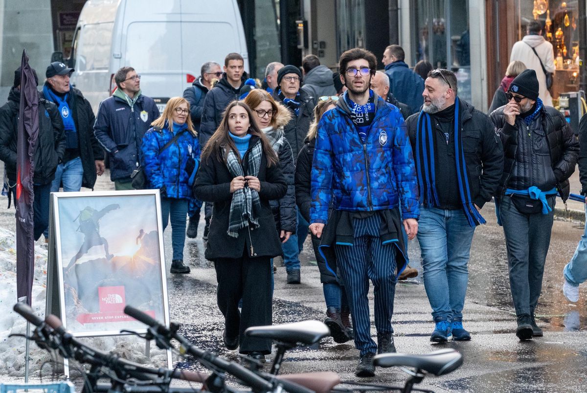 Eine Gruppe von Menschen, einige in blauen Jacken, geht auf einer städtischen Strasse. Fahrräder sind im Vordergrund.