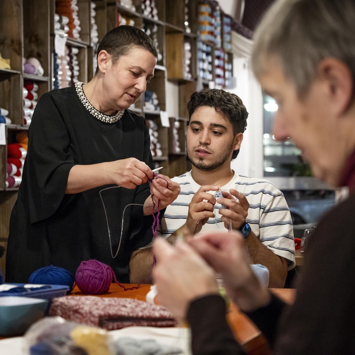 Participants apprenant le tricot et le crochet au Bar à Laine La Frange à Genève, entourés de pelotes colorées, le 13 novembre 2024.