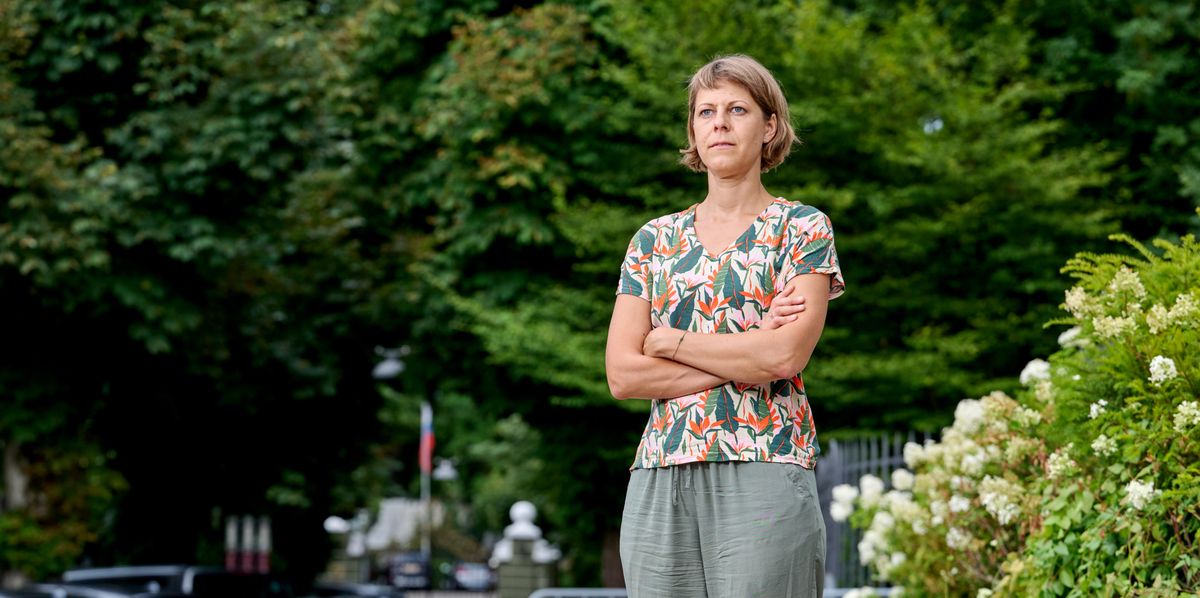 Frau mit verschränkten Armen steht auf einer Strasse, umgeben von grünen Bäumen und Sträuchern.