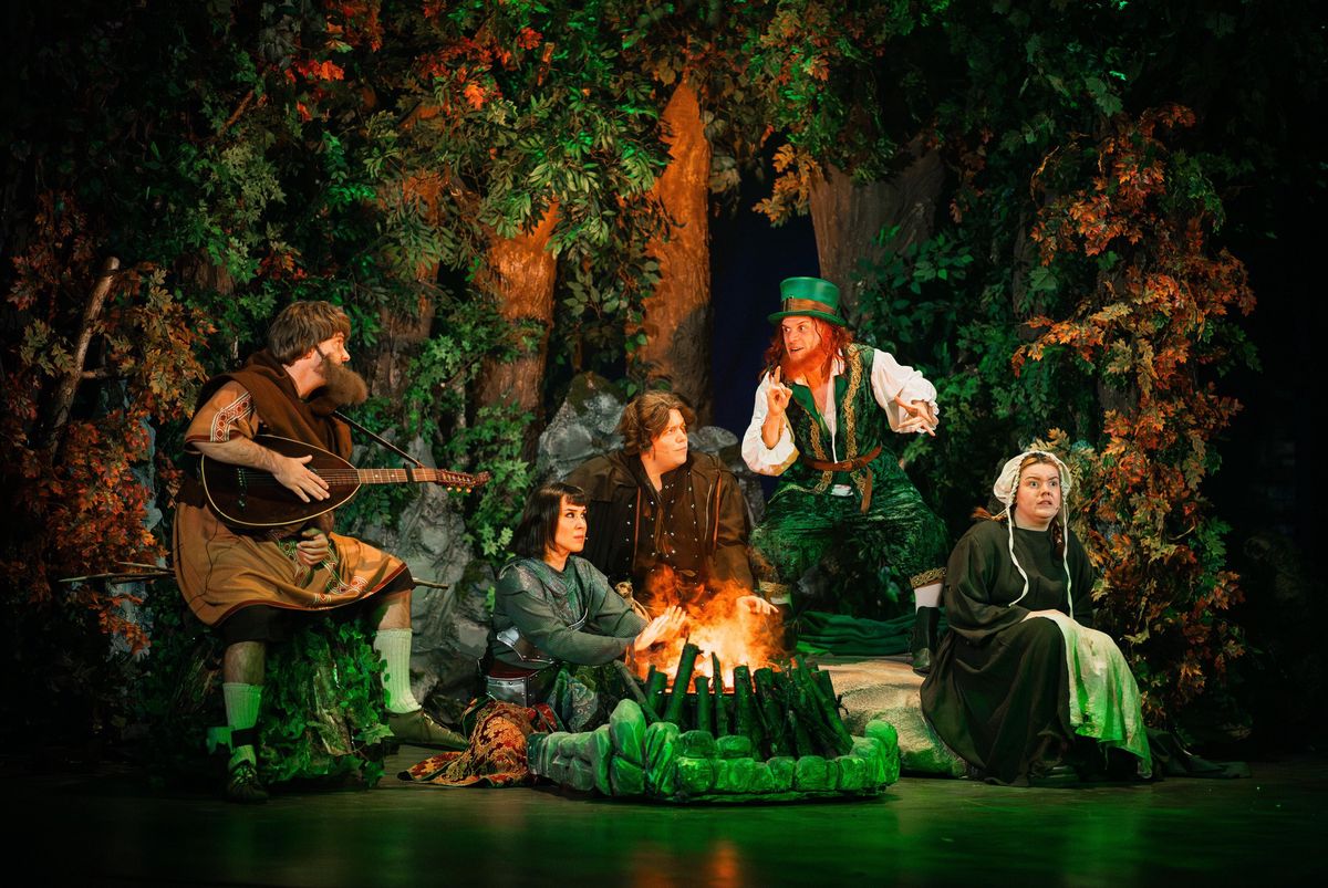 Scène de théâtre de Robin des Bois avec des personnages en costumes médiévaux réunis autour d’un feu de camp dans une forêt.