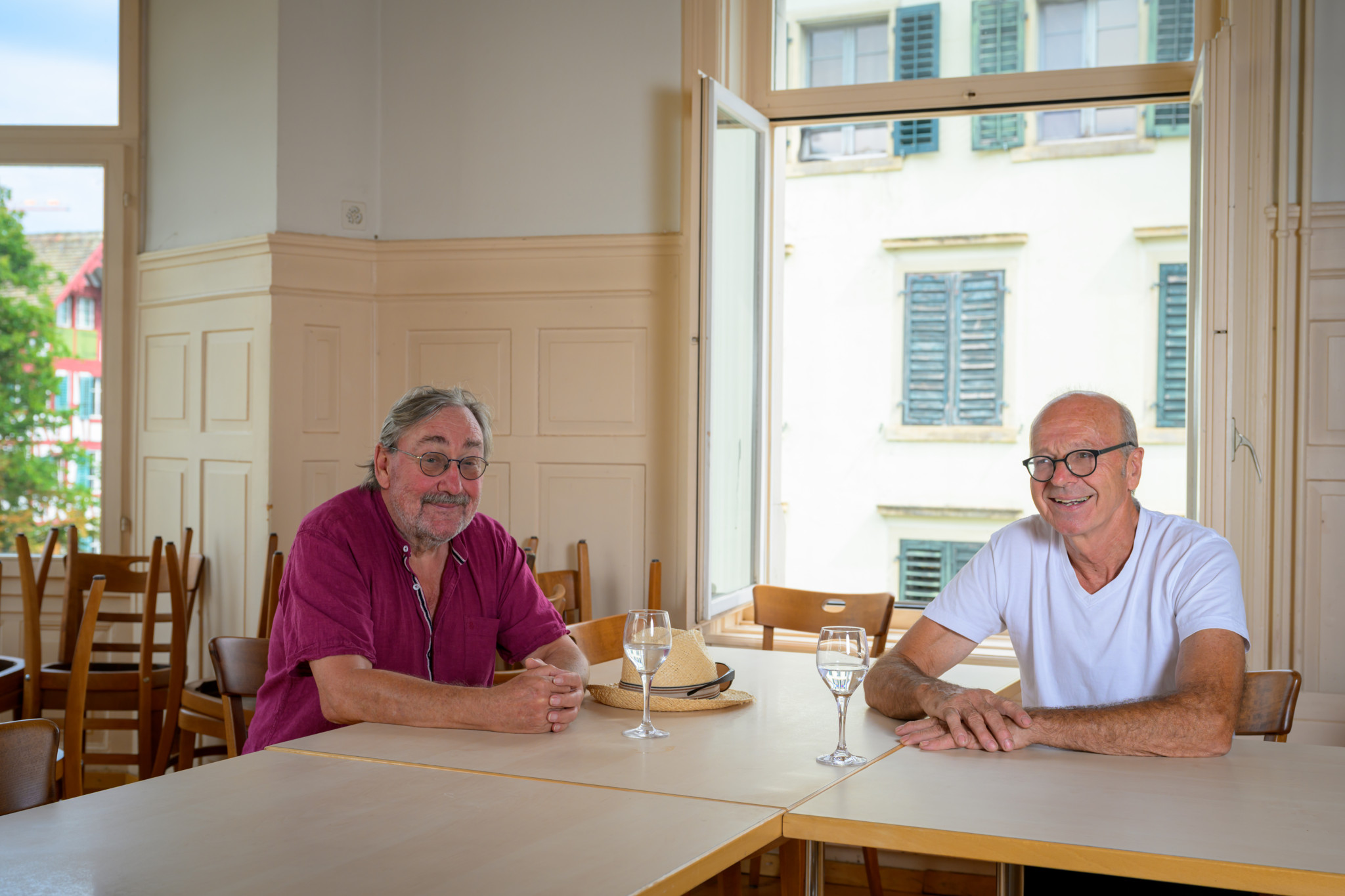 Ruedi Hotz (rosa Shirt) und Adrian Schärer (weisses Shirt) von der Volkshausgenossenschaft Wädenswil sitzen lächelnd am Tisch im Volkshaus.